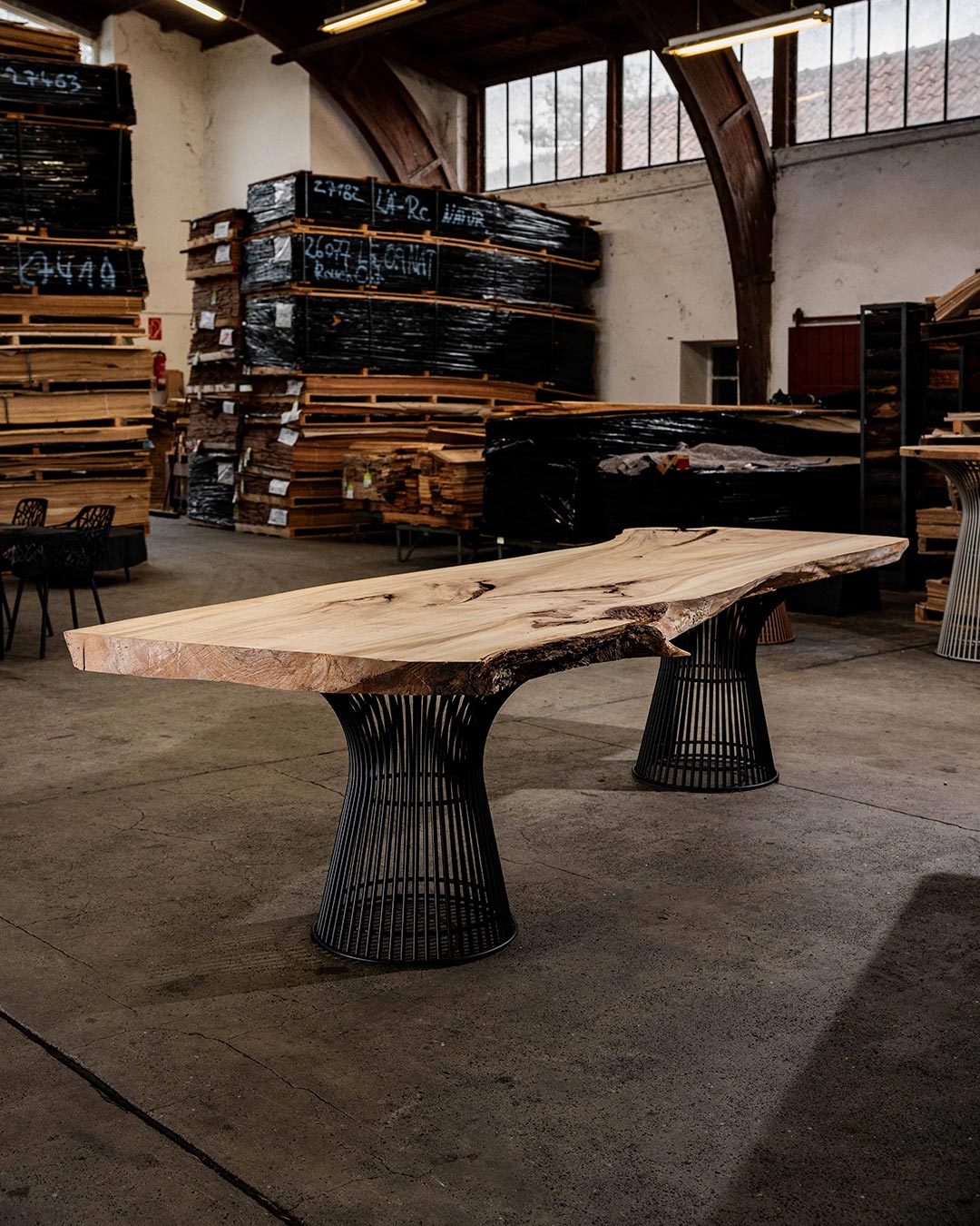 curveo Esstisch mit heller Massivholzplatte und natürlicher Baumkante auf zwei schwarzen Metallgestellen.