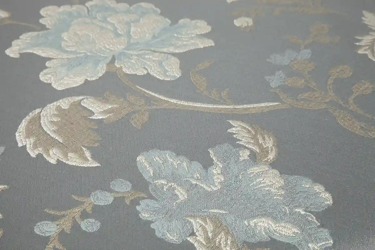 Polsterstoff in Blaugrau mit gewebtem floralem Muster aus hellblauen Blüten und beigefarbenen Ranken.